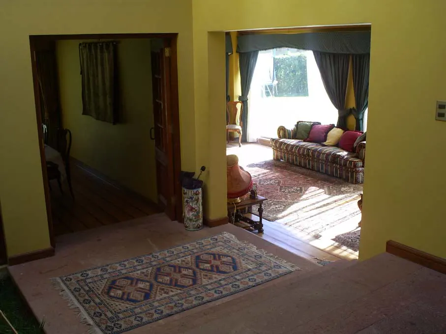 Interior view of a yellow-walled home with doorways leading to a living room with a patterned sofa and a room with a dark curtain. A patterned rug is on the floor.