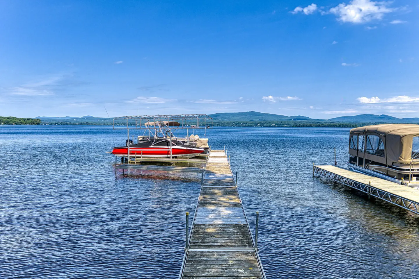 A long wooden dock leads to a red boat on a lake under a blue sky.