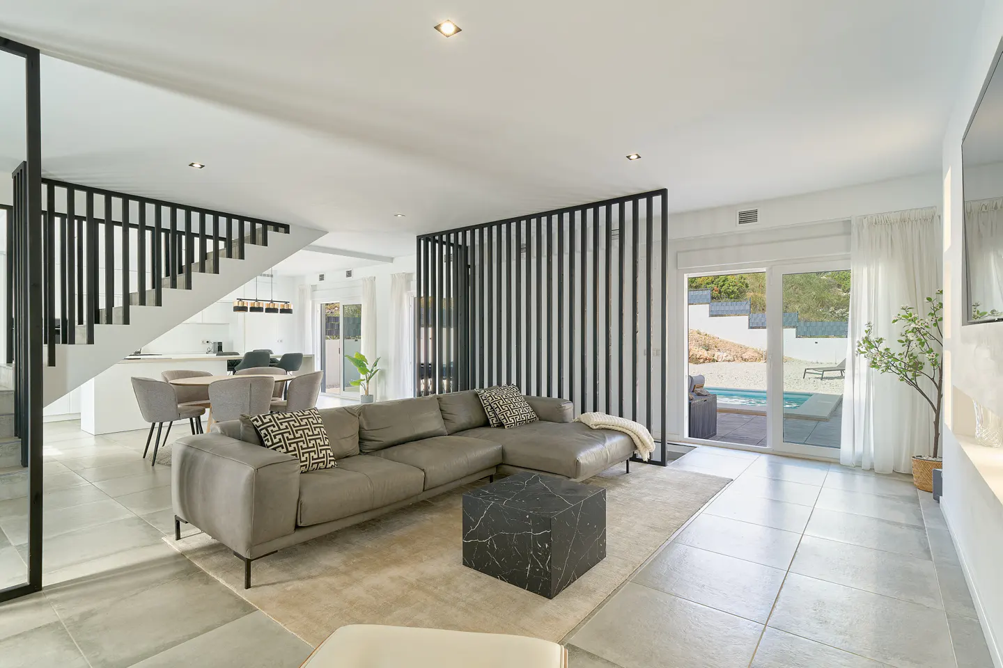 Bright, modern living room with a gray sectional sofa, black marble cube table, and a view of a pool through sliding glass doors.