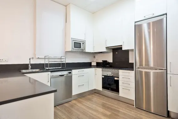 Modern kitchen with white cabinets, dark countertops, stainless steel appliances, and light wood-look flooring.