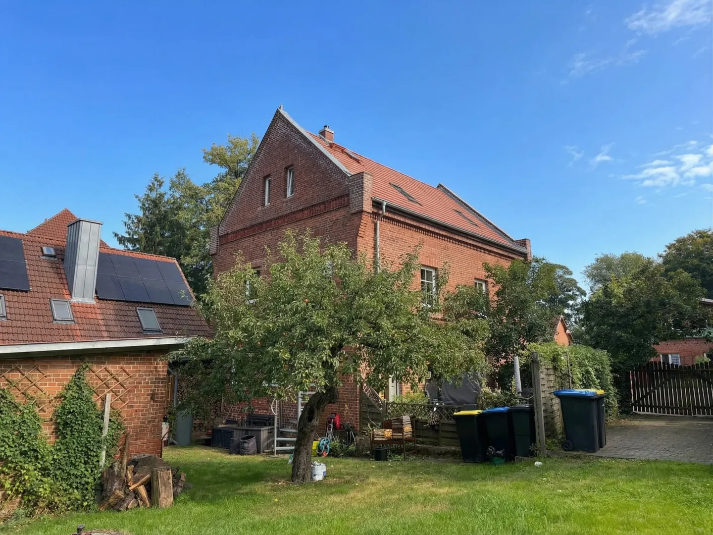 Exterior view of a two-story red brick house with a red tile roof, green lawn, and trees under a blue sky.