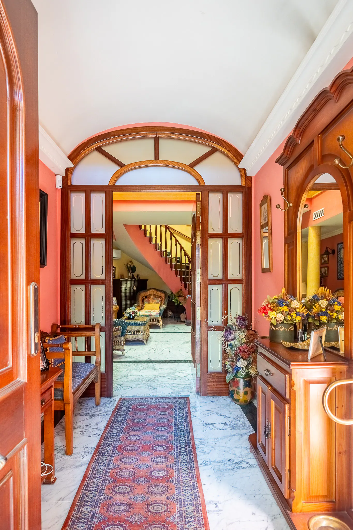 Open doorway into a home's foyer with marble floors, a red rug, and a wooden staircase in the background.