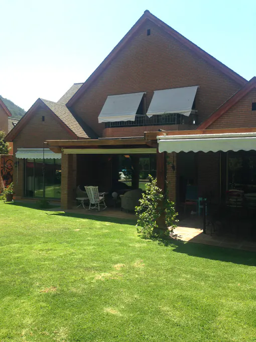 Brick house with a green lawn, covered patio with furniture, and white awnings.