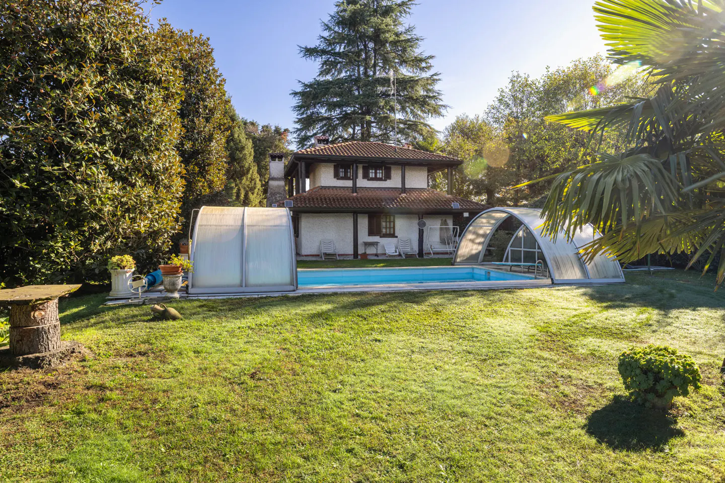 A backyard view of a two-story house with a pool and green lawn on a sunny day.