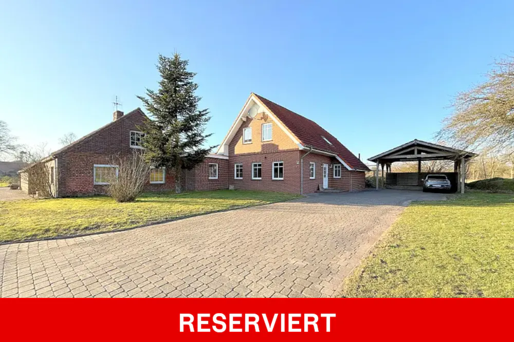 Exterior view of a brick house with a red tile roof, a carport, and a paved driveway. "RESERVIERT" text overlay.