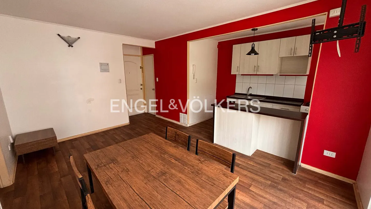 A real estate photo shows a dining area with a wooden table and chairs, a kitchen with white cabinets, and red accent walls.