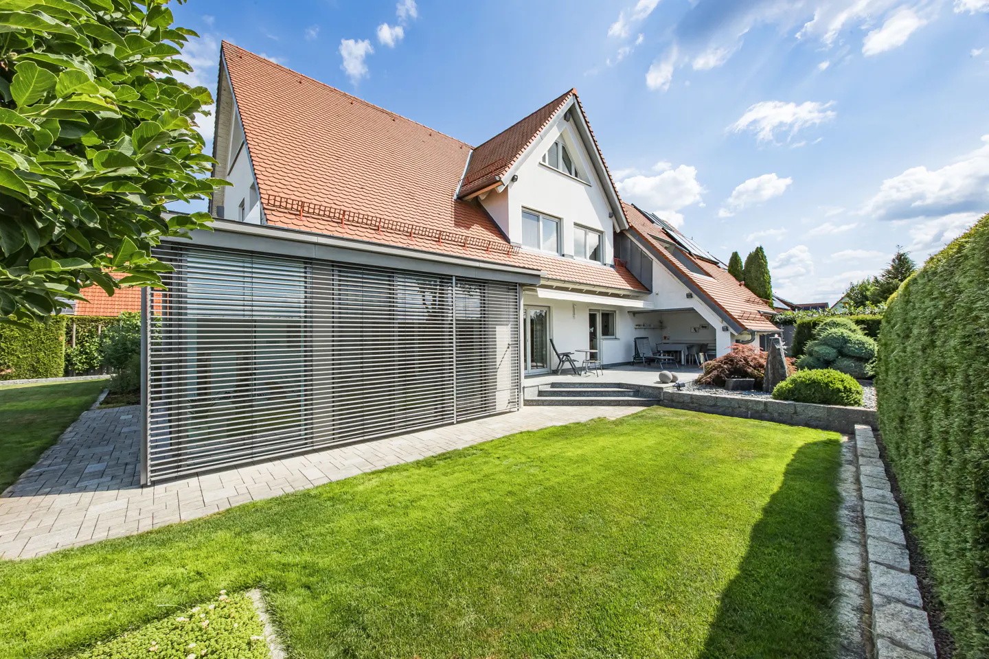 Exterior view of a white house with a red tile roof, a green lawn, and a patio with outdoor furniture.