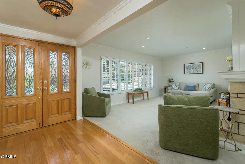 A bright living room with hardwood floors, a double door entry, and green armchairs.
