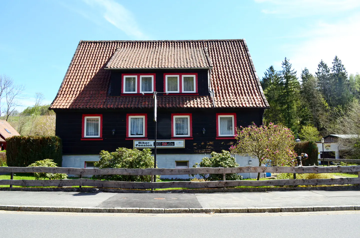 A two-story black house with a red-tiled roof, white-trimmed windows, and a wooden fence in front under a blue sky.