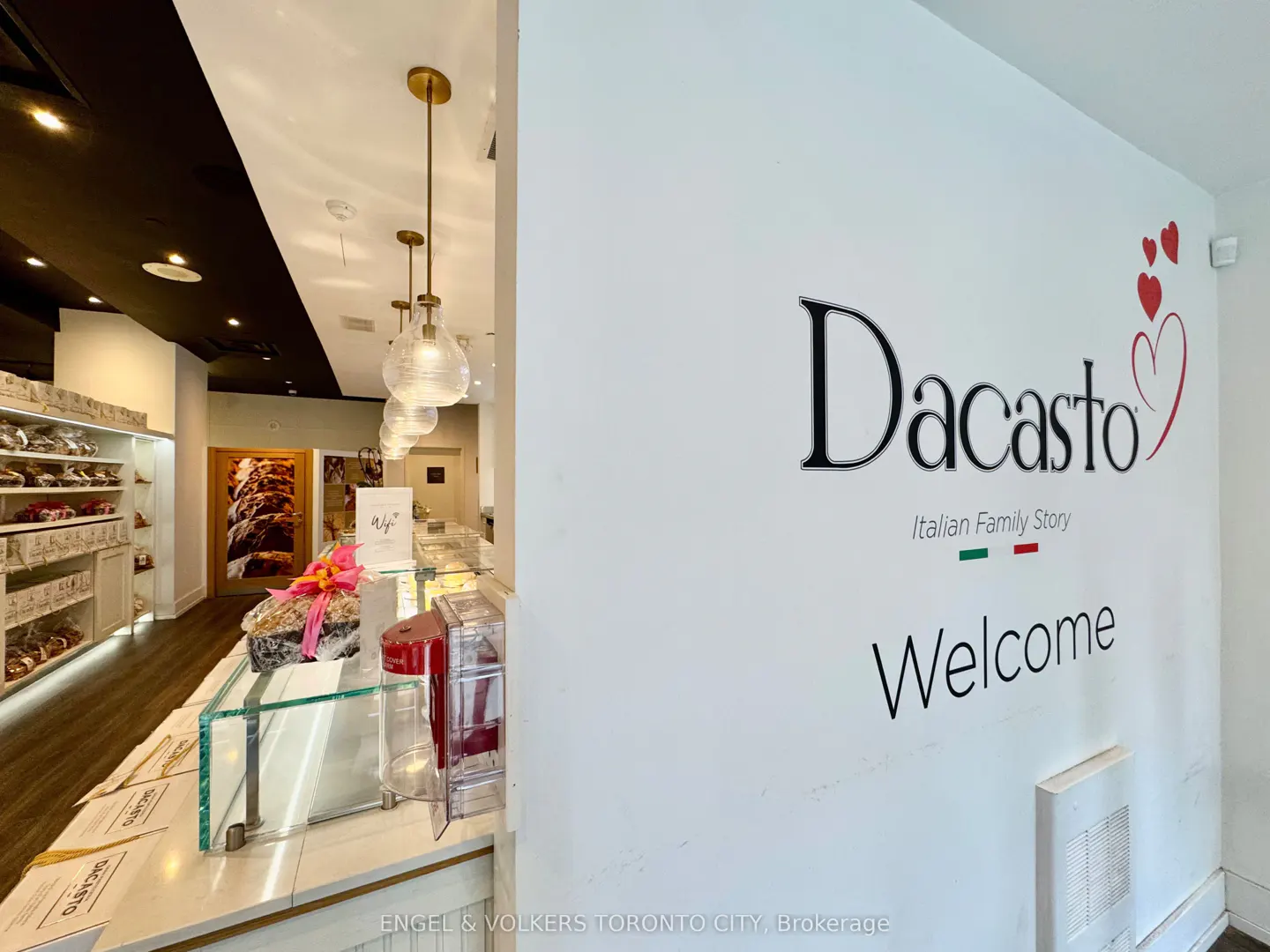 Interior view of Dacasto bakery with white walls, glass display case, and shelves stocked with baked goods.