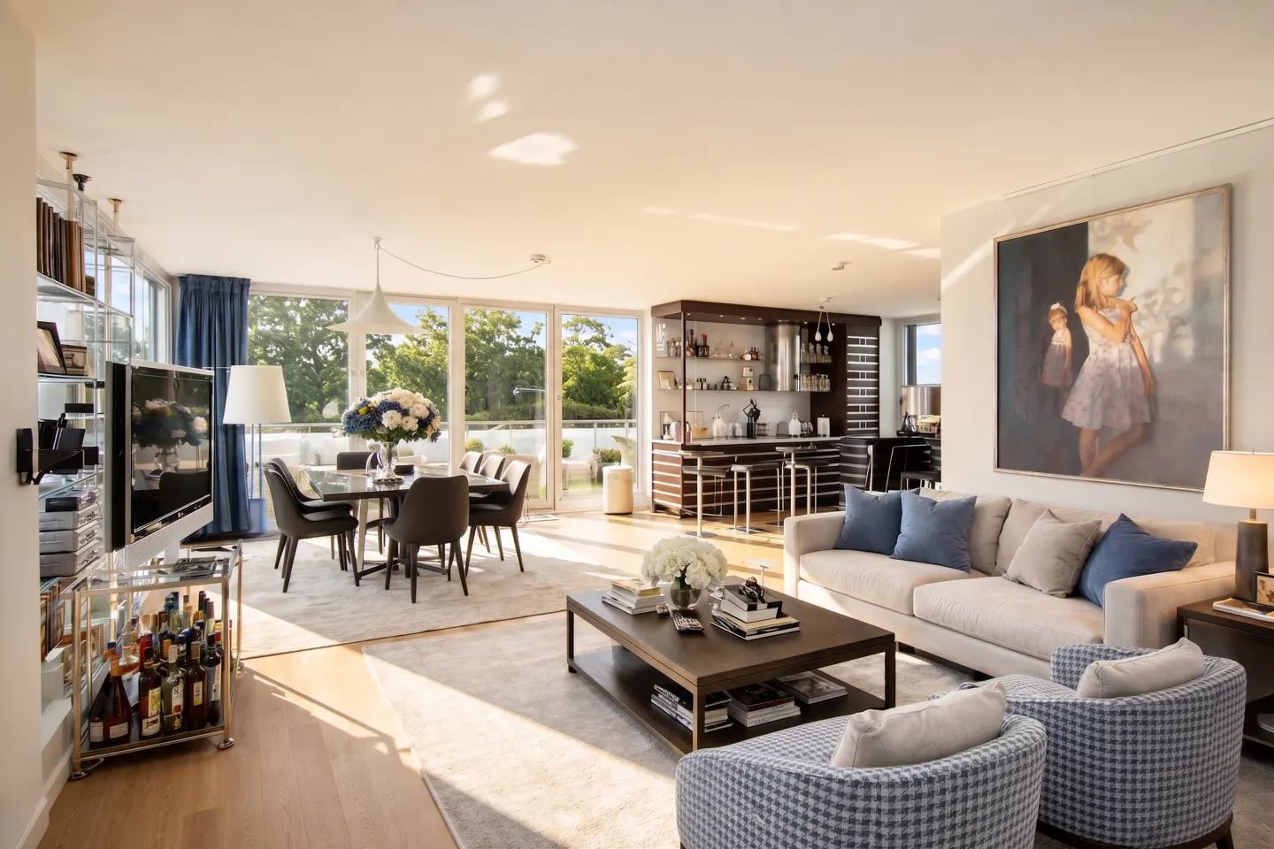 Bright, open-concept living space with dining table, bar, sofa, and armchairs. Large windows offer a view of trees. A painting hangs above the sofa.