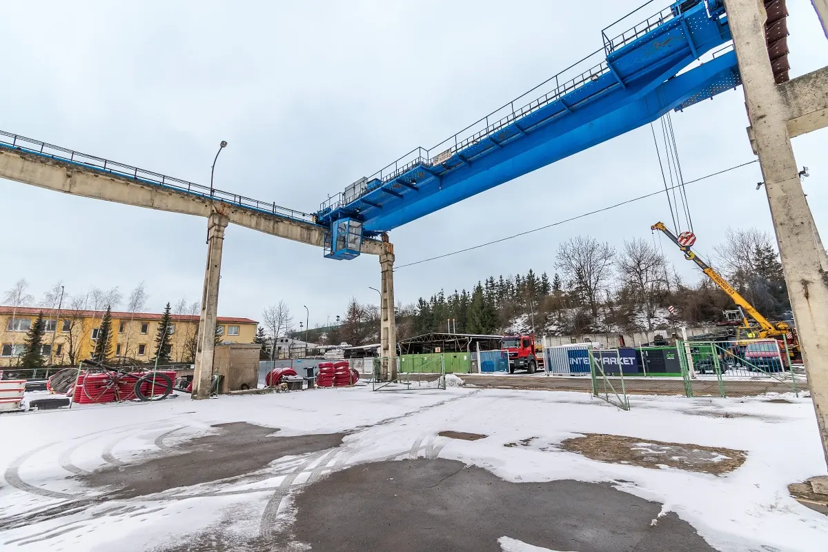 Outdoor shot of a blue gantry crane over a snowy lot with a yellow crane in the background.