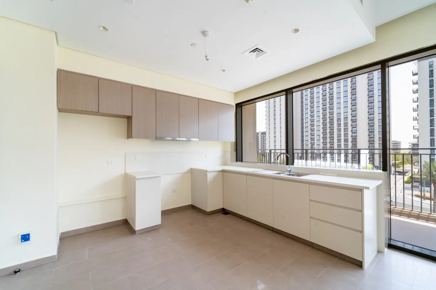 Modern kitchen with light wood upper cabinets, white lower cabinets, and large windows overlooking a city building.