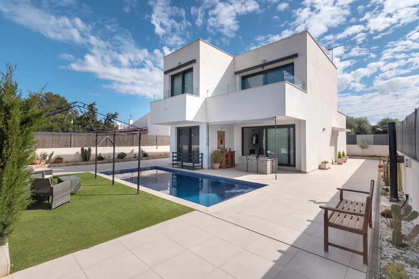 Modern two-story white house with a blue swimming pool, patio, and green lawn under a partly cloudy sky.