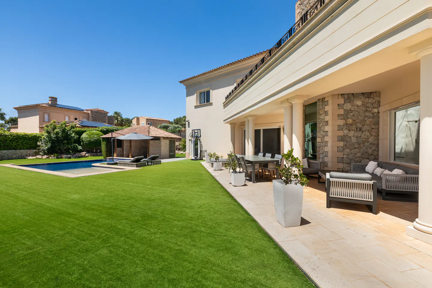 Backyard view of a luxury home with a pool, patio, and green lawn on a sunny day.
