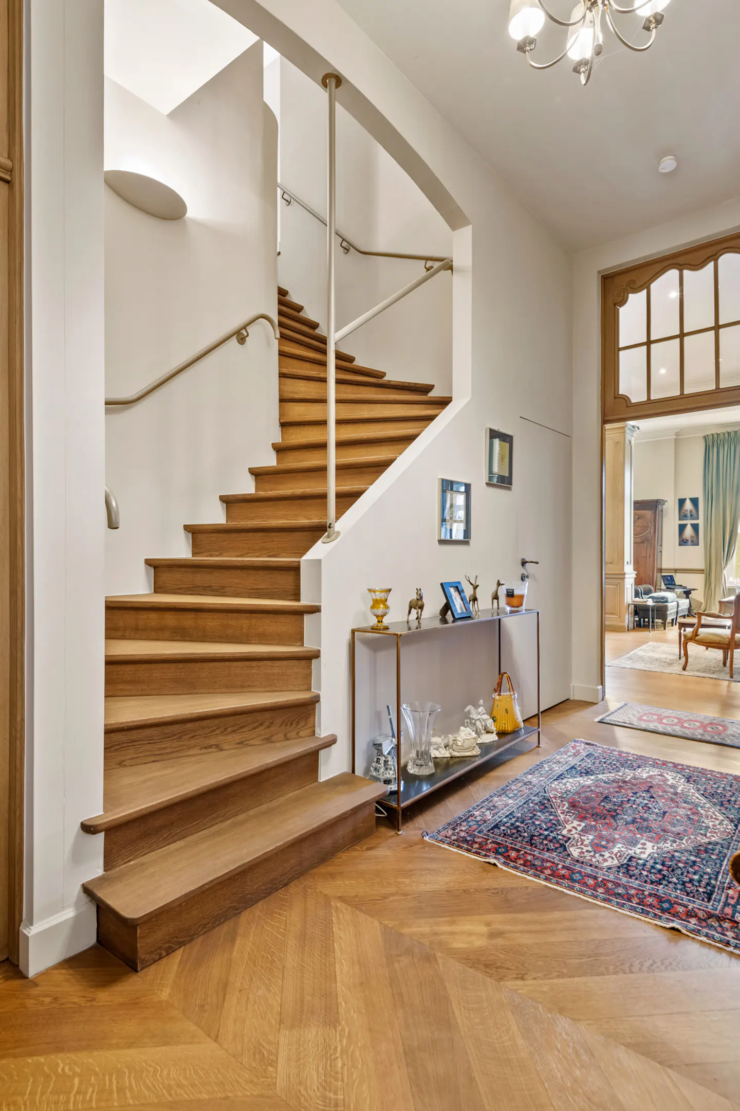 Bright foyer with wood floors, staircase, and open doorway to a living room. A console table displays decorative items.