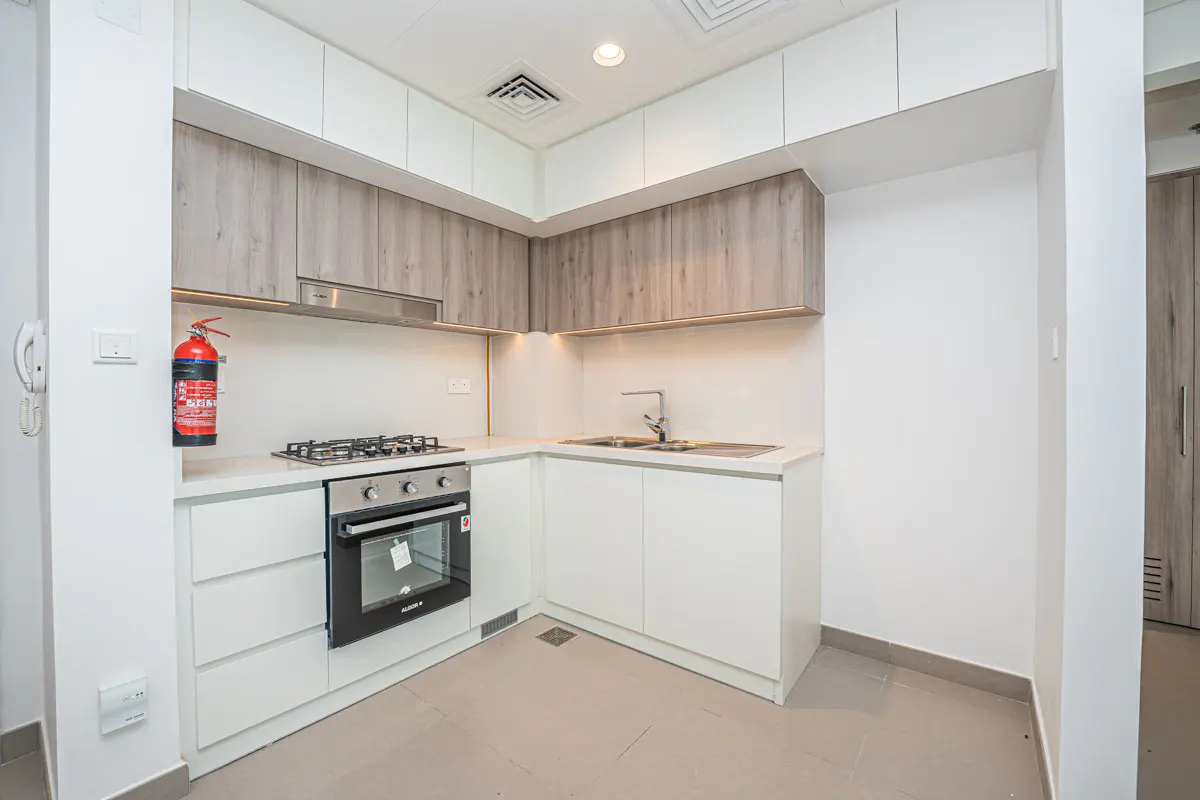 Modern kitchen with white lower cabinets, wood-tone upper cabinets, built-in oven, gas stove, and a red fire extinguisher.