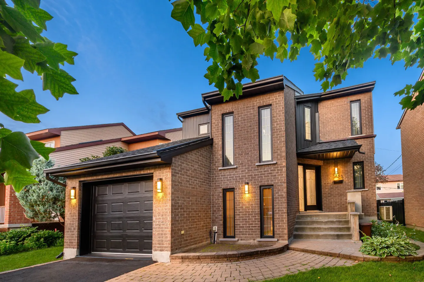 Modern two-story brick home with a single garage, paved walkway, and warm exterior lighting at dusk.