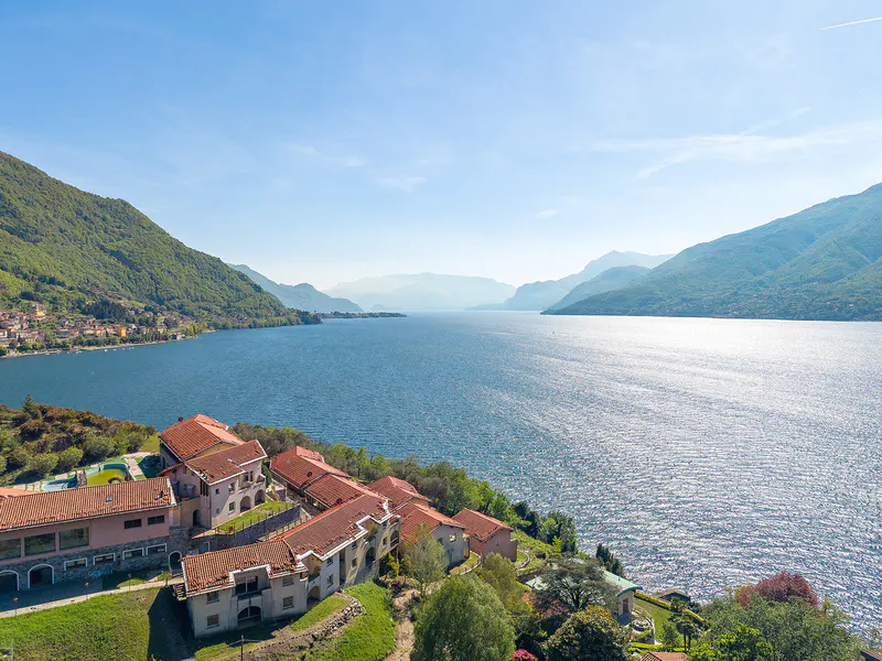 Scenic view of Lake Como, Italy, with mountains, blue water, and buildings with red tile roofs on a green hillside.