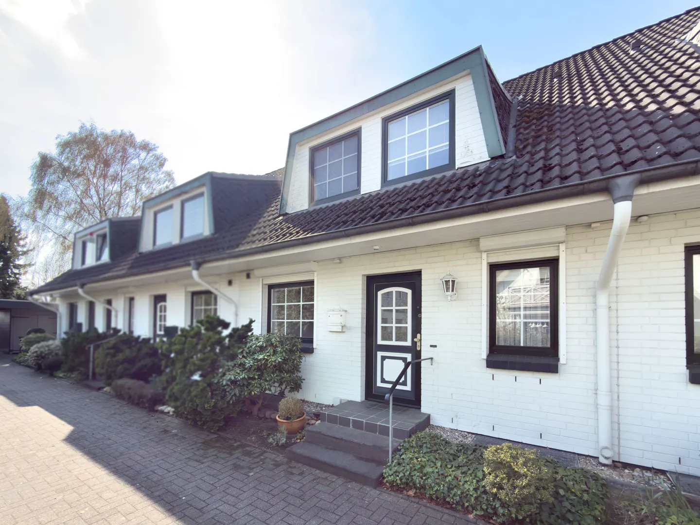 Exterior view of a white brick townhouse with black trim, dormer windows, and a brick walkway.