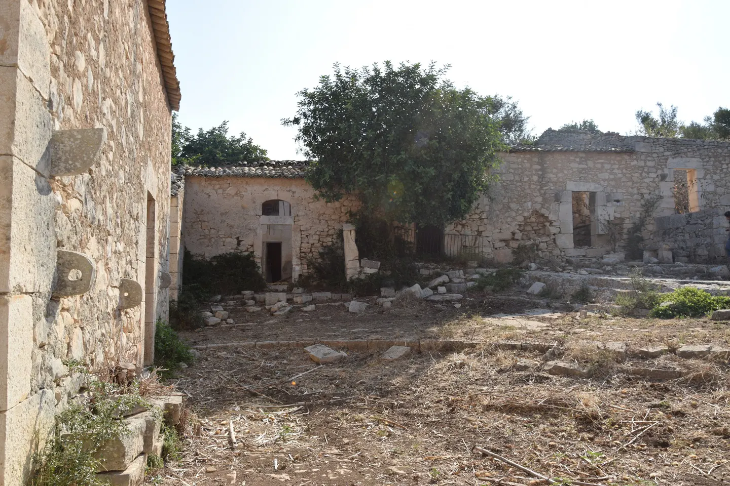 Exterior view of a stone building with open doorways and a tree in the courtyard.