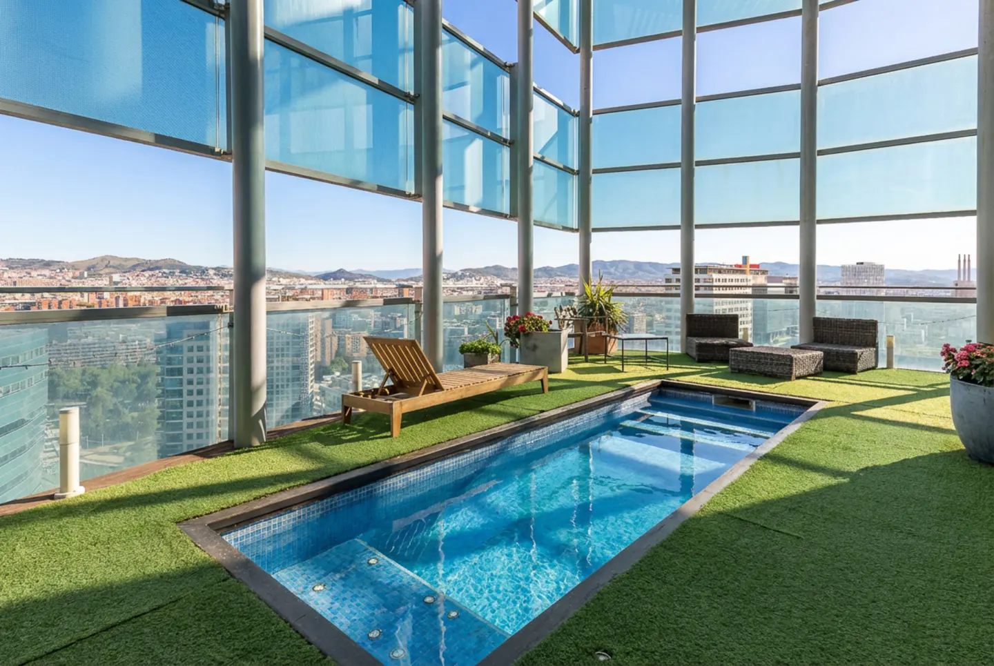 Rooftop pool with city view. Blue tiled pool on green turf, surrounded by lounge chair, potted plants, and wicker furniture.