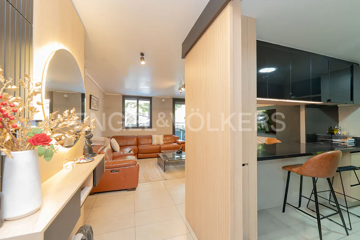 A modern apartment interior with a brown leather sofa, kitchen island with stools, and a decorative mirror.