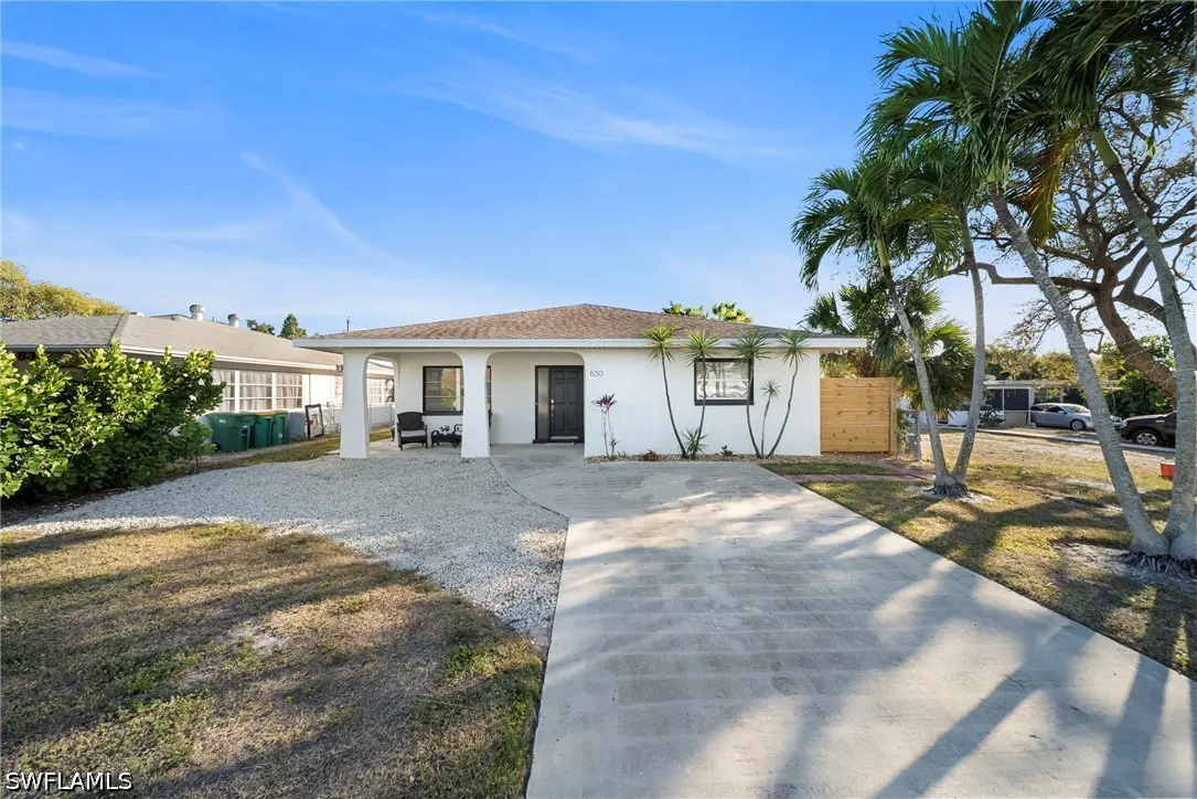 Front view of a one-story white house with a gray driveway and palm trees on a sunny day.