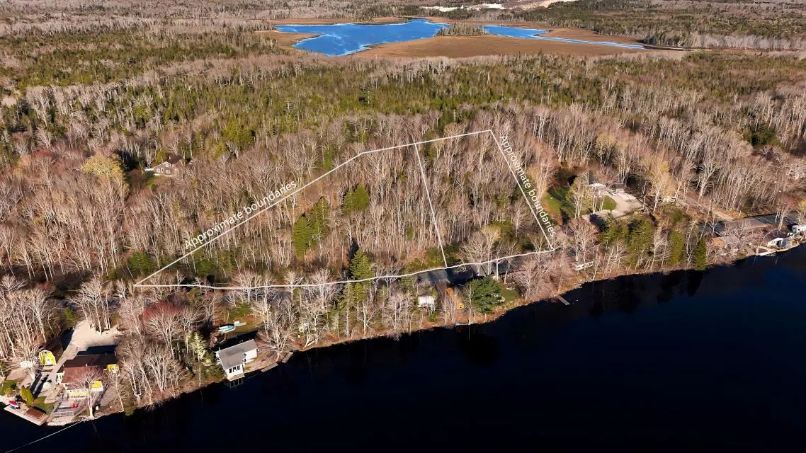 Aerial view of a wooded lot with approximate boundaries outlined in white, bordering a dark blue lake. A smaller lake is visible in the background.