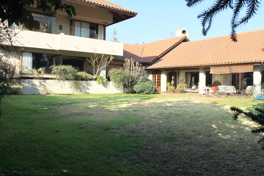Two-story house with a large green lawn, beige walls, and a red tile roof on a sunny day.