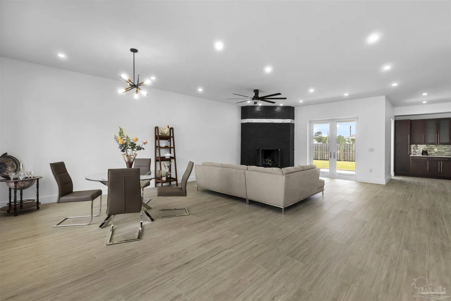 Open-concept living space with a dining table, beige sofa, and black fireplace. Wood-look tile flooring and white walls.