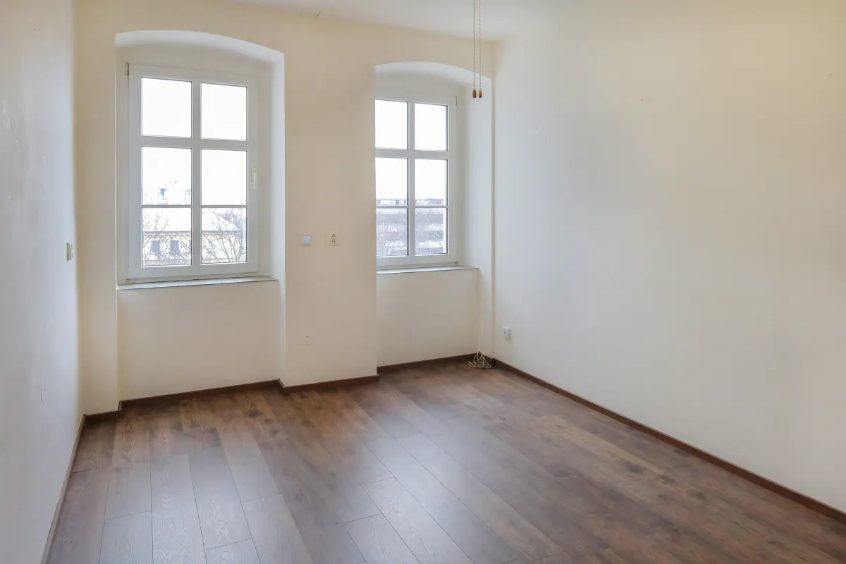 Empty room with cream walls, dark wood-look flooring, and two arched windows letting in natural light.