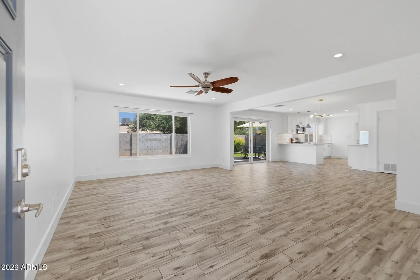 Bright, open-concept living room with light wood-look tile floors, white walls, a ceiling fan, and a view of the kitchen.