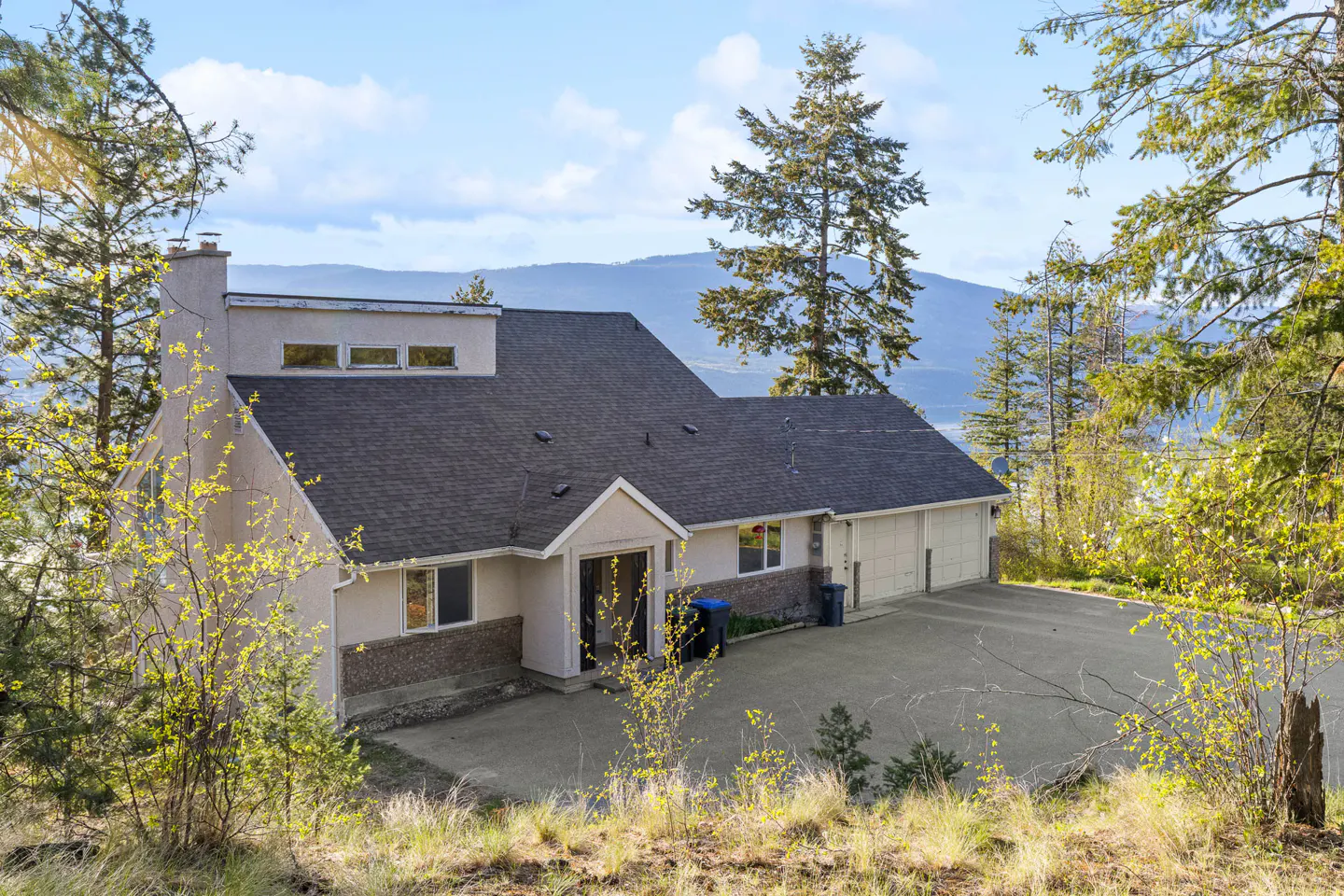Exterior view of a two-story house with a gray roof, beige siding, and a two-car garage, surrounded by trees.