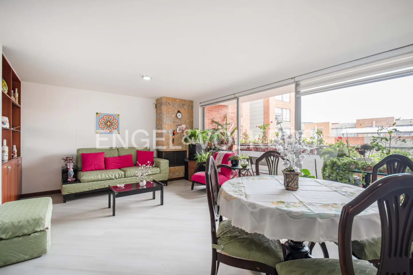 Bright living room with green sofa, pink cushions, round table, and balcony with plants. Engel & Völkers logo visible.