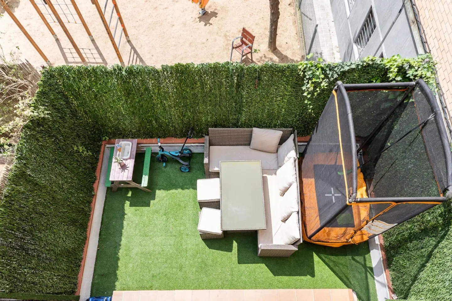 Aerial view of a backyard with green artificial turf, a picnic table, a patio set, a child's scooter, and a trampoline.