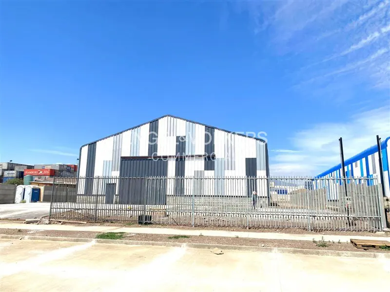 Exterior of a gray and white metal warehouse with a fence in front, under a blue sky.