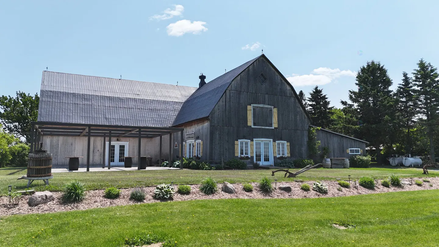 Exterior of a gray barn-style building with yellow shutters and a covered patio, surrounded by green grass and trees.