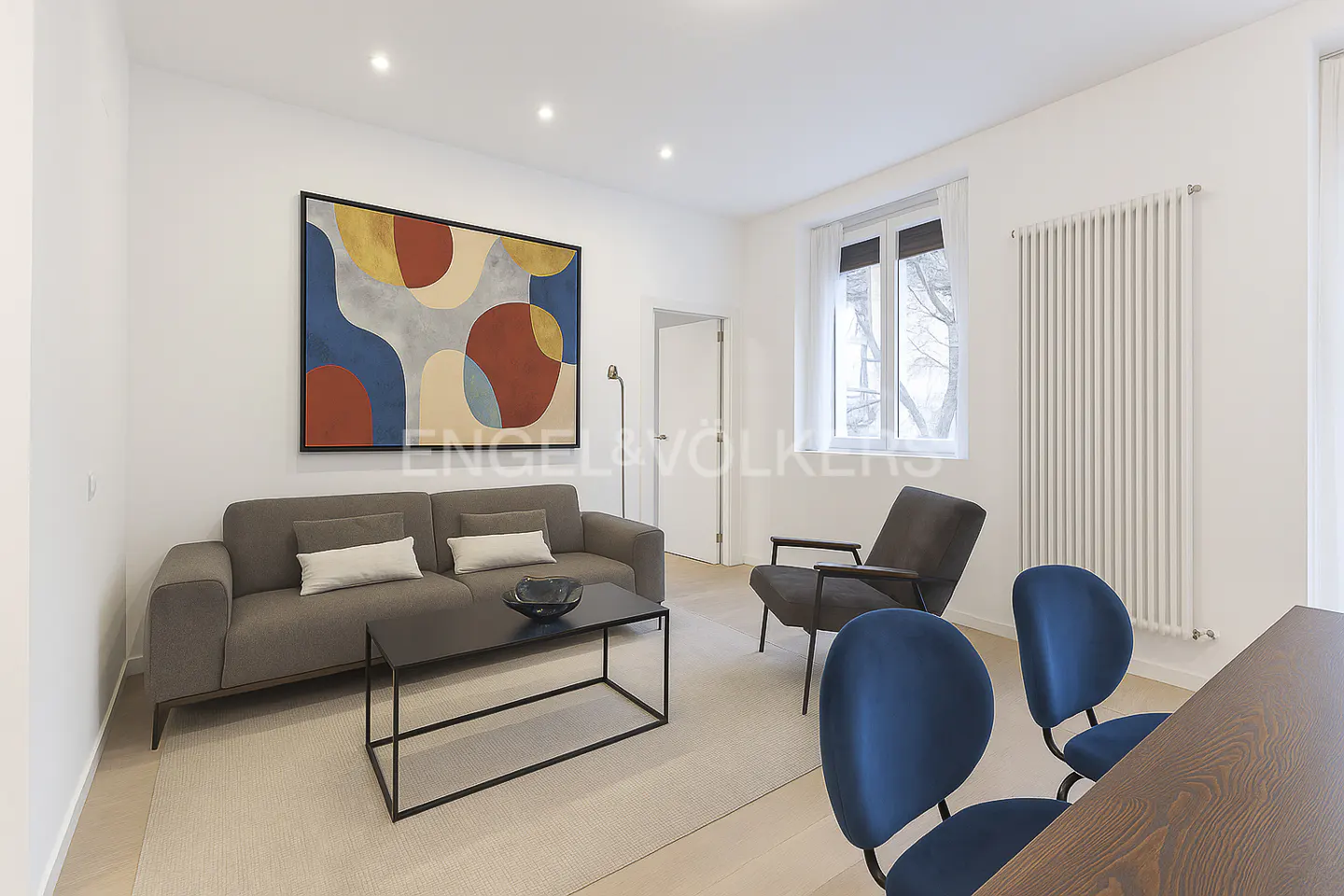 Living room with a gray sofa, black coffee table, blue chairs, and an abstract painting on a white wall.