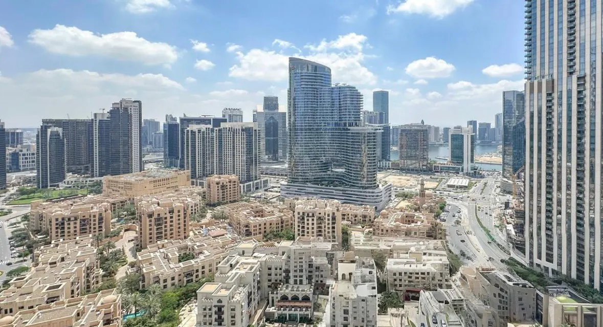 Cityscape view of Dubai with modern buildings, roads, and a blue sky with white clouds.