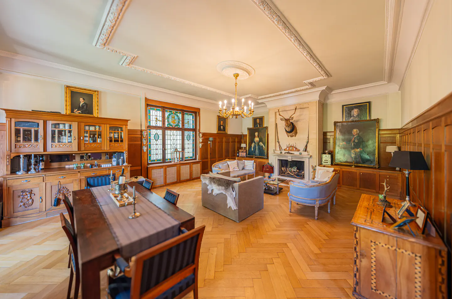 A spacious living room with wood paneling, a fireplace, portraits, and a dining table.