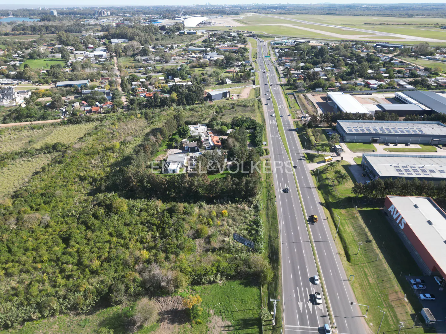 Aerial view of a property with lush greenery next to a highway with cars and an airport in the background.