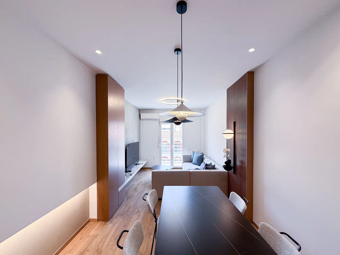 A modern apartment interior with a black dining table, chairs, and a living room with a sofa and TV in the background.