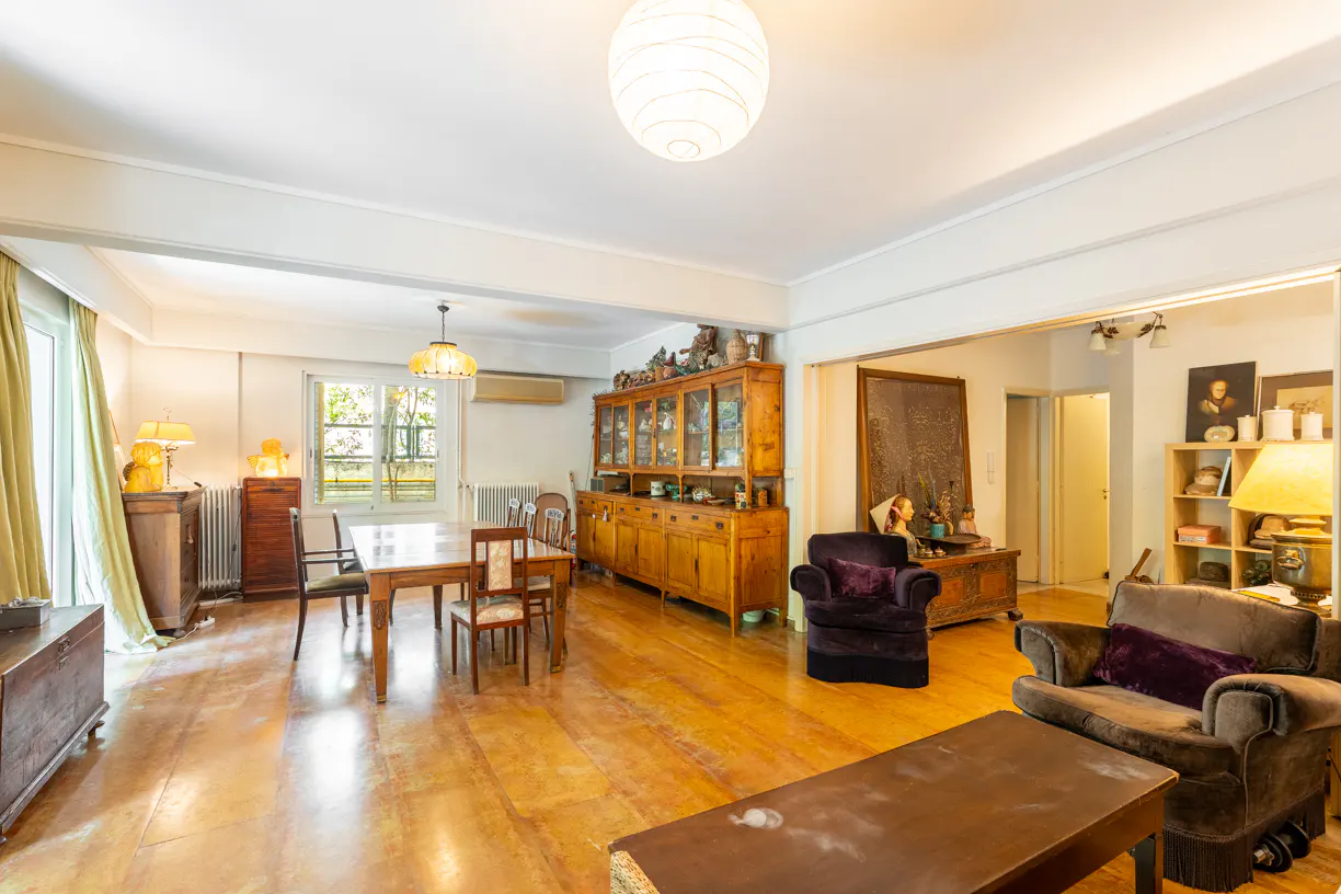 A wide shot of a living and dining room with wood floors, furniture, and a large china cabinet.