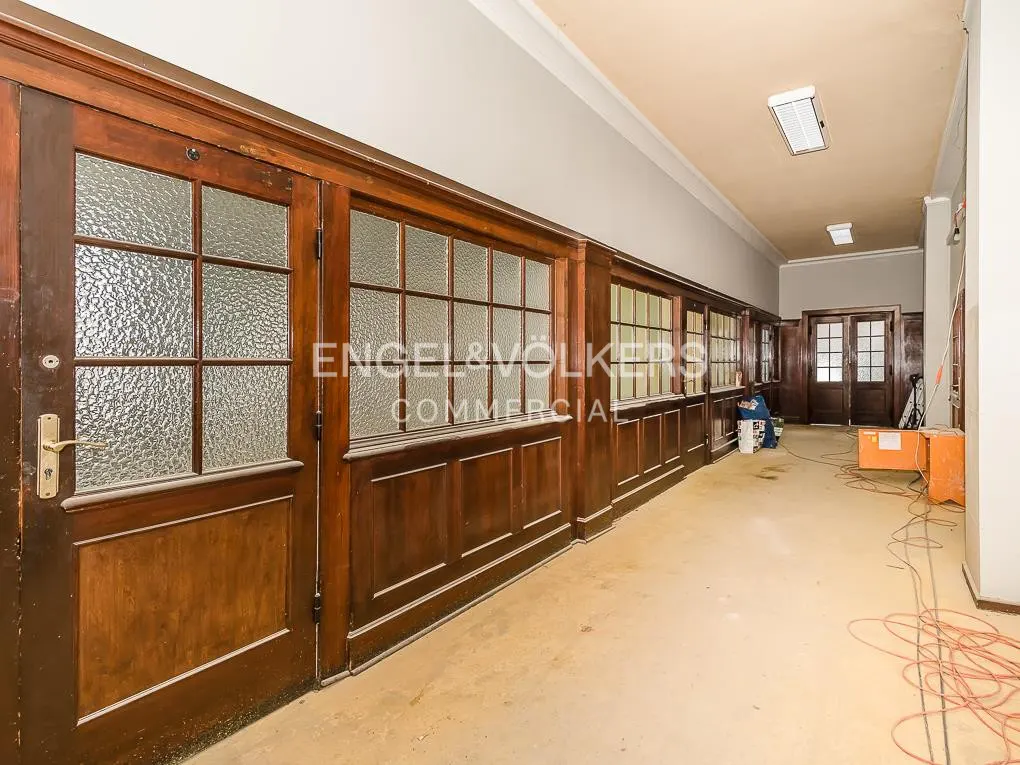 Hallway with wood-framed glass doors and windows, beige walls and floor, and the Engel & Völkers Commercial logo on the glass.
