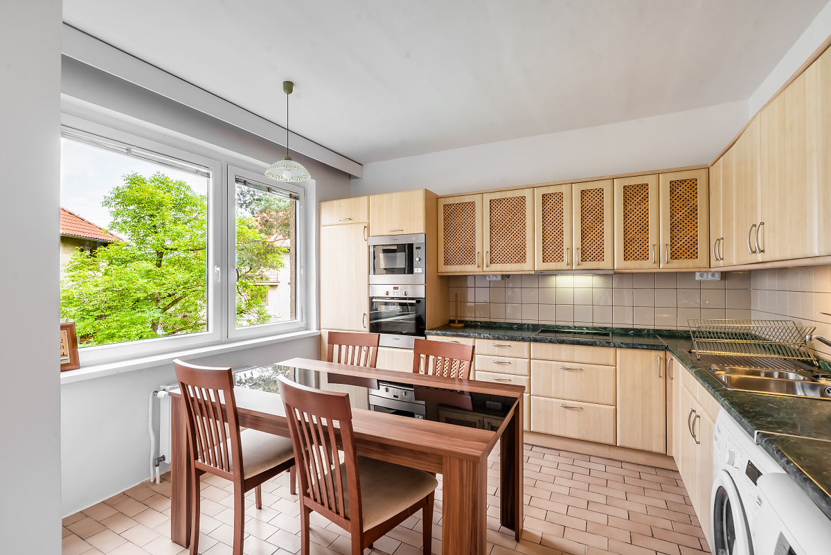 Kitchen with light wood cabinets, dark countertops, a dining table with four chairs, and a window overlooking green trees.