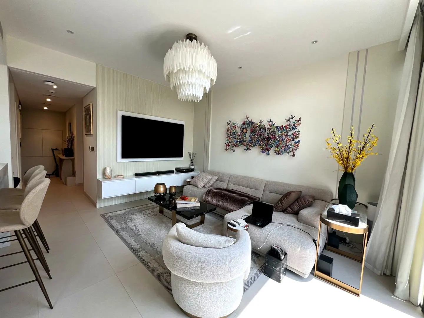 Modern living room with a beige sectional, white armchair, wall-mounted TV, and a large white tiered chandelier.
