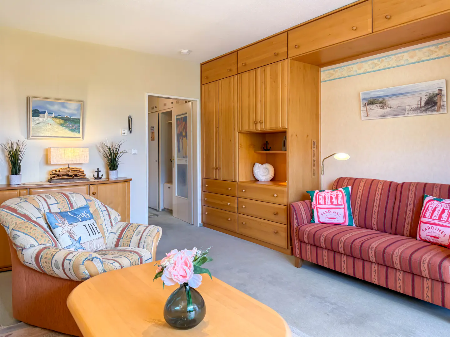 Living room with a striped sofa, patterned armchair, and light wood built-in cabinets. A coffee table with flowers sits in the foreground.