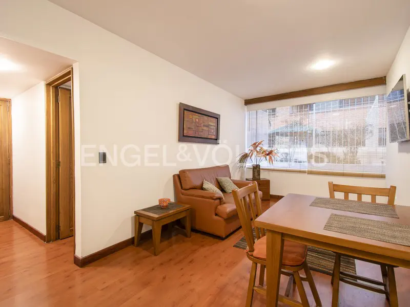 Living room with a brown leather sofa, wooden dining table, and hardwood floors, featuring a large window with blinds.