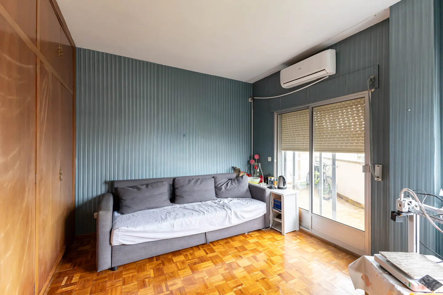 Living room with a gray sofa, blue striped walls, and parquet flooring. A sliding glass door leads to a balcony.